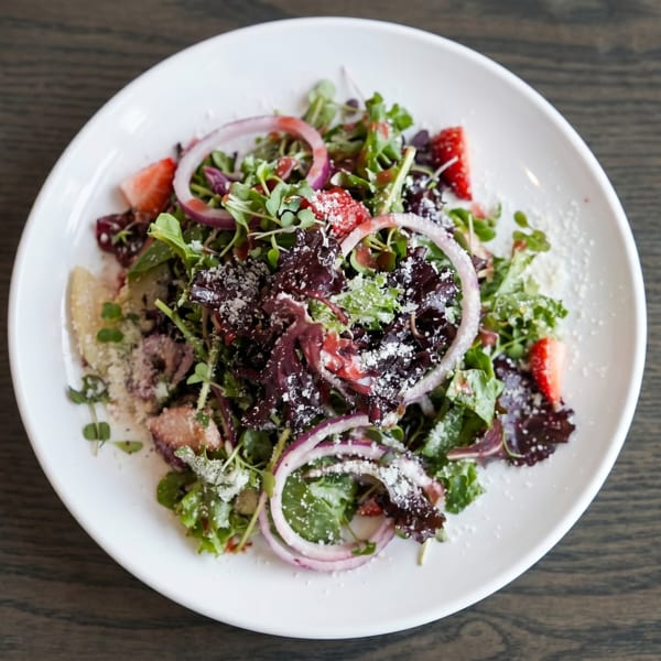 Fresh salad with mixed greens, red onions, strawberries, and grated cheese on a white plate.