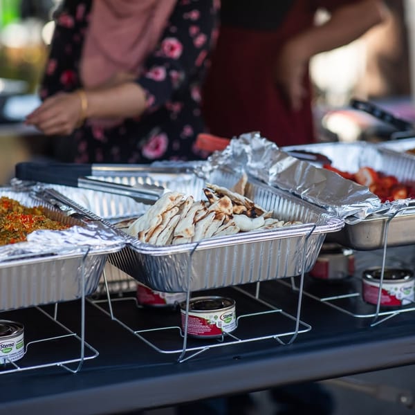 Buffet line with foil pans of rice, flatbread, and strawberries, with people in background.