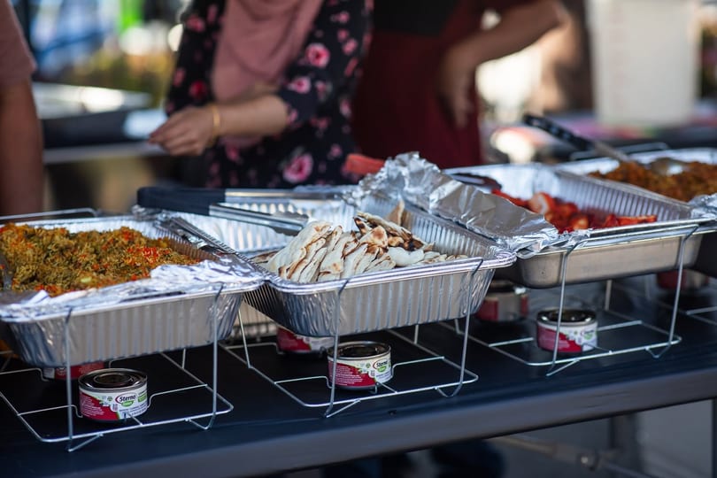 Buffet line with foil pans of rice, flatbread, and strawberries, with people in background.