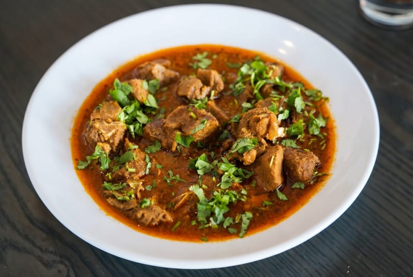 A white bowl filled with a rich, red curry, garnished with fresh green cilantro.