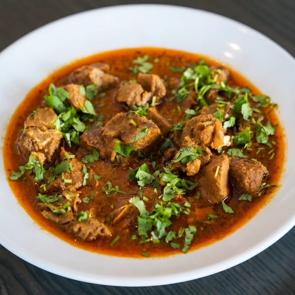 A white bowl filled with a rich, red curry, featuring chunks of meat and fresh green cilantro.