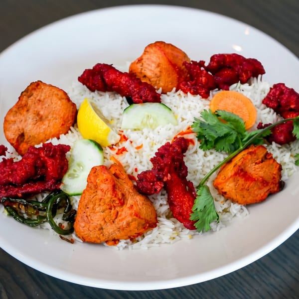 White plate with rice, red and orange chicken pieces, lemon, cucumber, and cilantro.