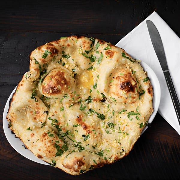 Garlic naan bread with melted butter and fresh cilantro on a white plate with a knife.